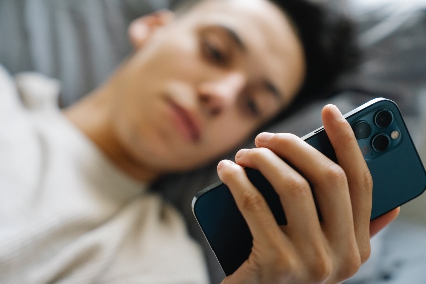 Jonge jongen ligt op bed met telefoon in hand